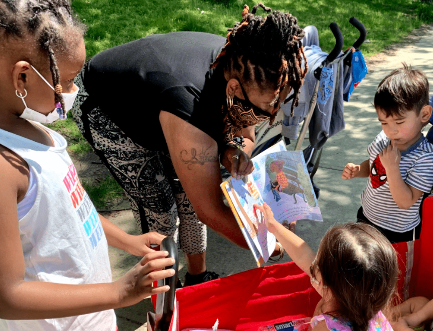 Women reading a book to children outside