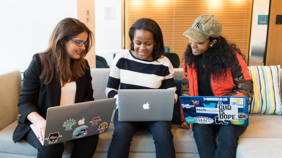 Three people sitting together on their laptops, collaborating 