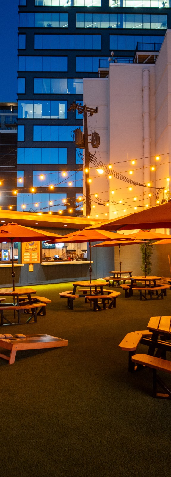 Backyard at Odie's, picnic tables with umbrellas open at night with fairy lights strung over and Nashville in background