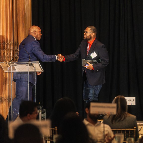 Man shaking another man's hand while on stage accepting an award