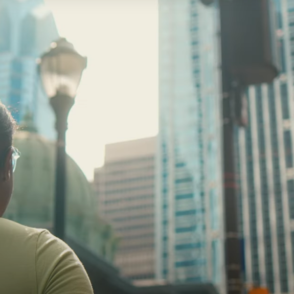 The back of a womens head as she looks at a tall skyscraper in the city