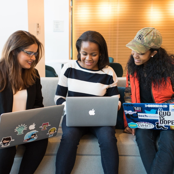 Three people sitting together on their laptops, collaborating 