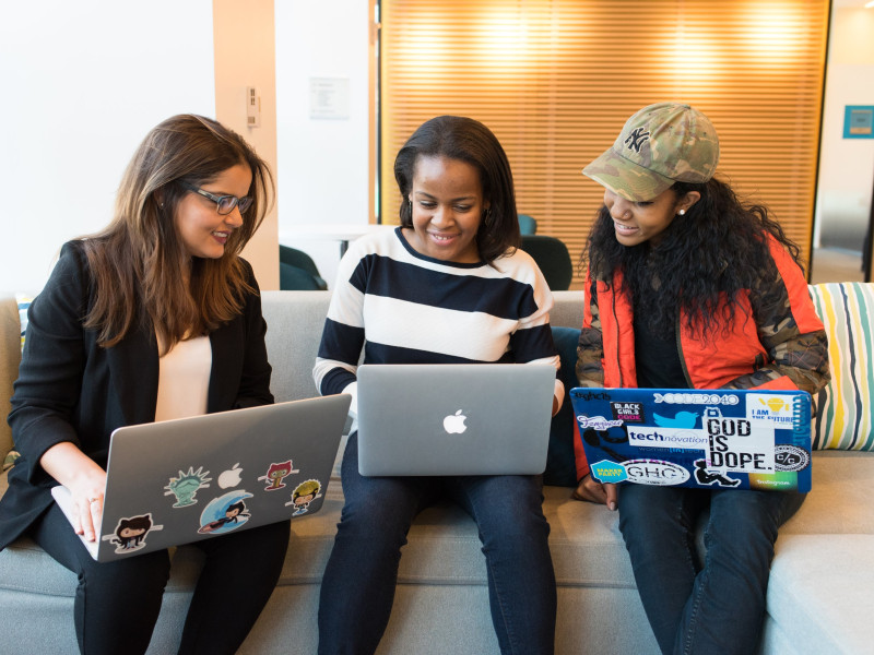 Three people sitting together on their laptops, collaborating 