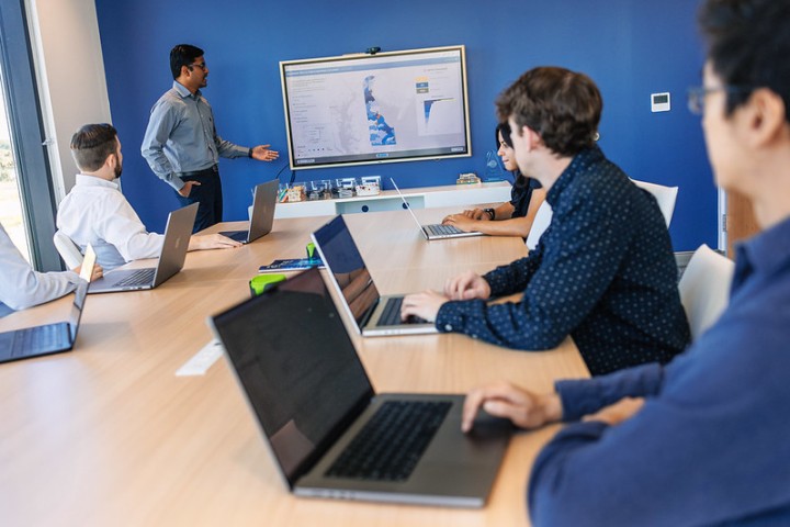 Three men sitting at a board room table looking at a screen with a map on it
