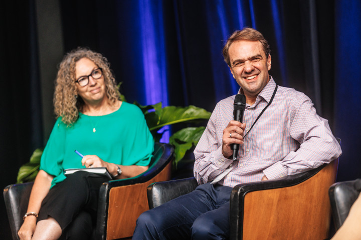 Two colleagues sitting on chairs on a stage with microphones