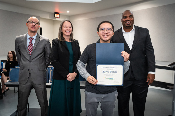 A graduate holding up a certificate with a small group of professionals