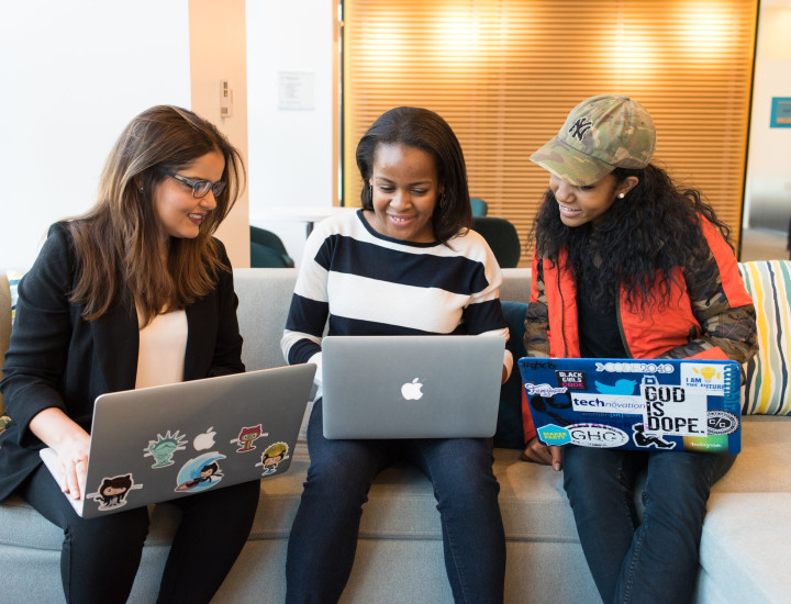 Three people sitting together on their laptops, collaborating 
